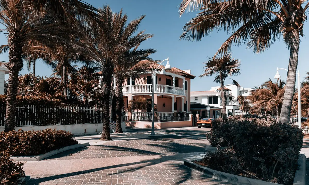 House with a balcony behind palm trees on a sunny street