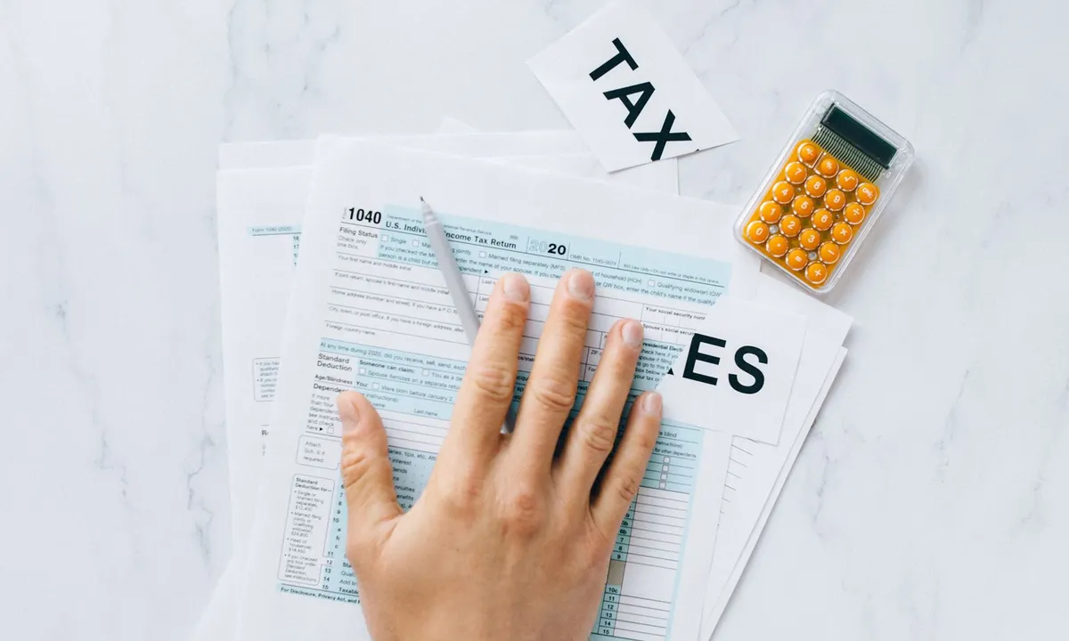Hand resting on a Form 1040 tax return next to a calculator and cards spelling “TAXES”