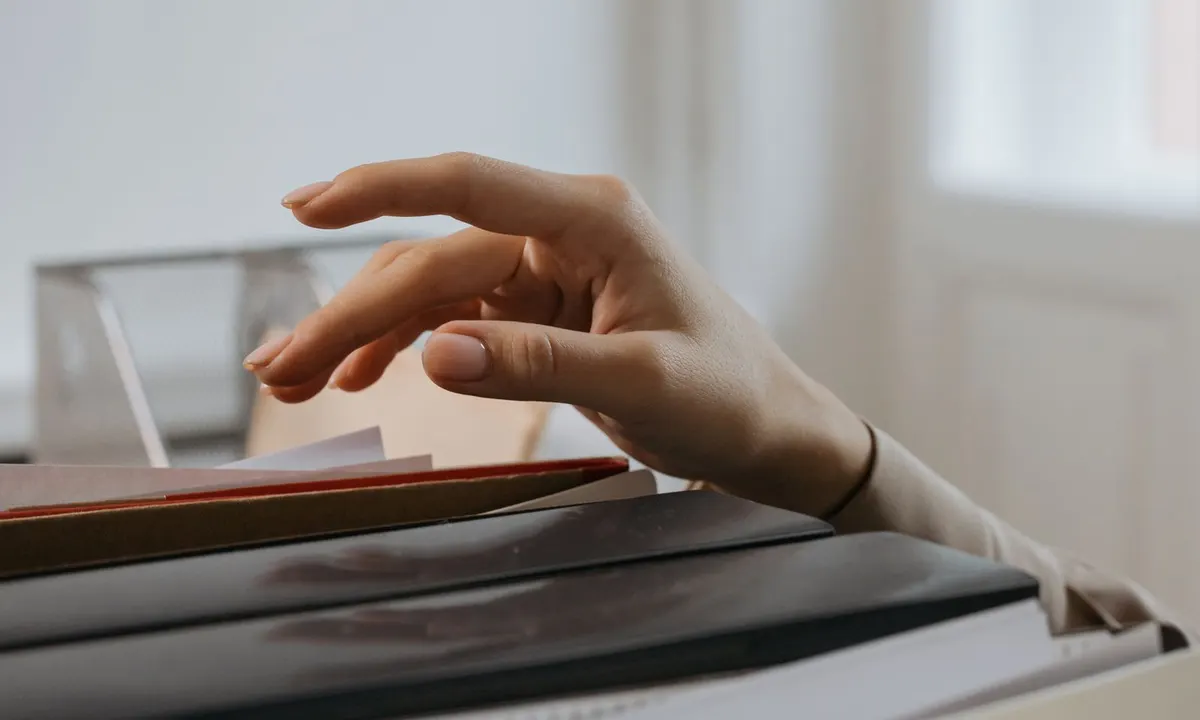 A hand reaching for a file folder in a stack of office records