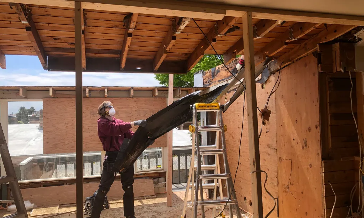 Worker in a dust mask removing an old beam during a home renovation with exposed framing