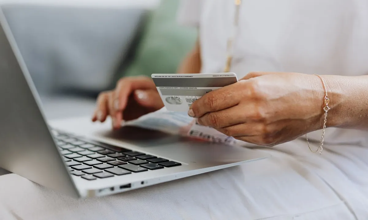 Hands holding a payment card over a laptop keyboard while paying a bill online