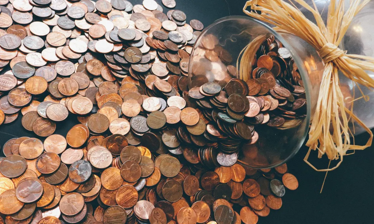U.S. pennies spilling out of a tipped glass jar onto a dark table