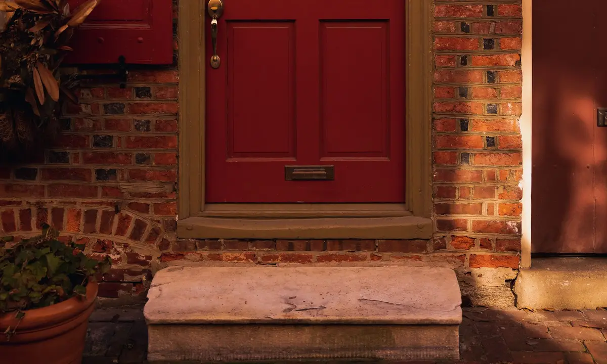 Red front door of a brick row house above stone steps