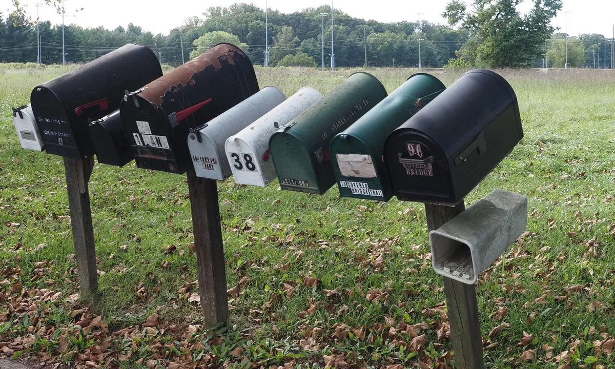 A row of rural roadside mailboxes on wooden posts with fallen autumn leaves in the grass
