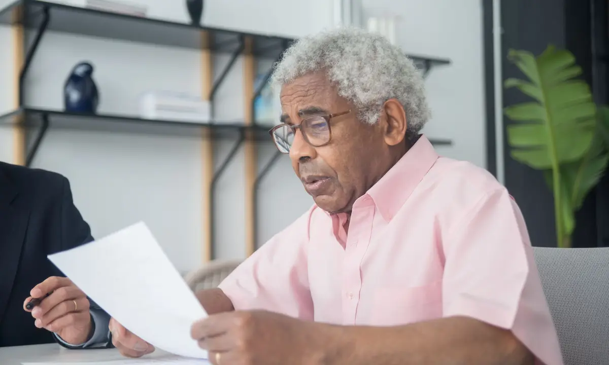 Older man in glasses reading a document at a table