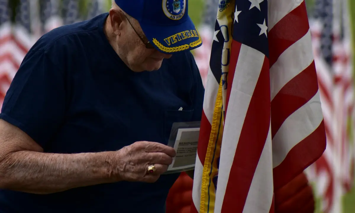 Veteran in a cap reading a card beside an American flag