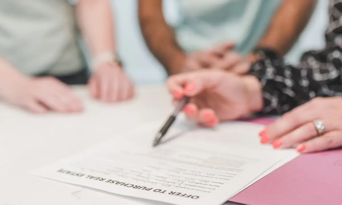 Hands signing a real estate purchase offer at a table