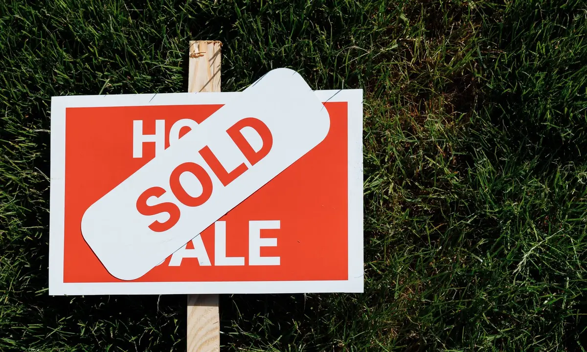 Sold sticker across a home for sale sign on a lawn