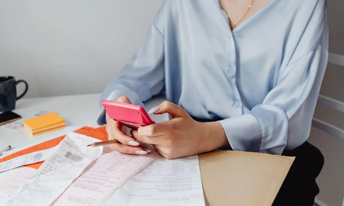 Woman using a calculator over a pile of household bills and receipts